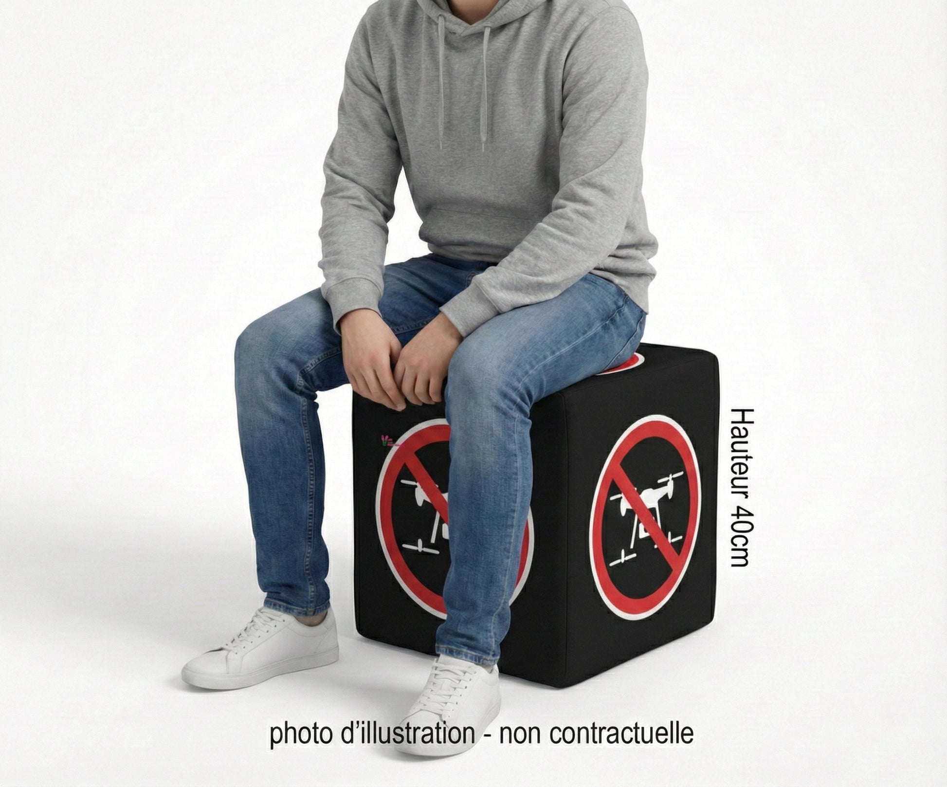 Cube personnalisable anti-drone noir avec symboles d'interdiction de survol en rouge et blanc, une personne est assise dessus lors d'une exposition