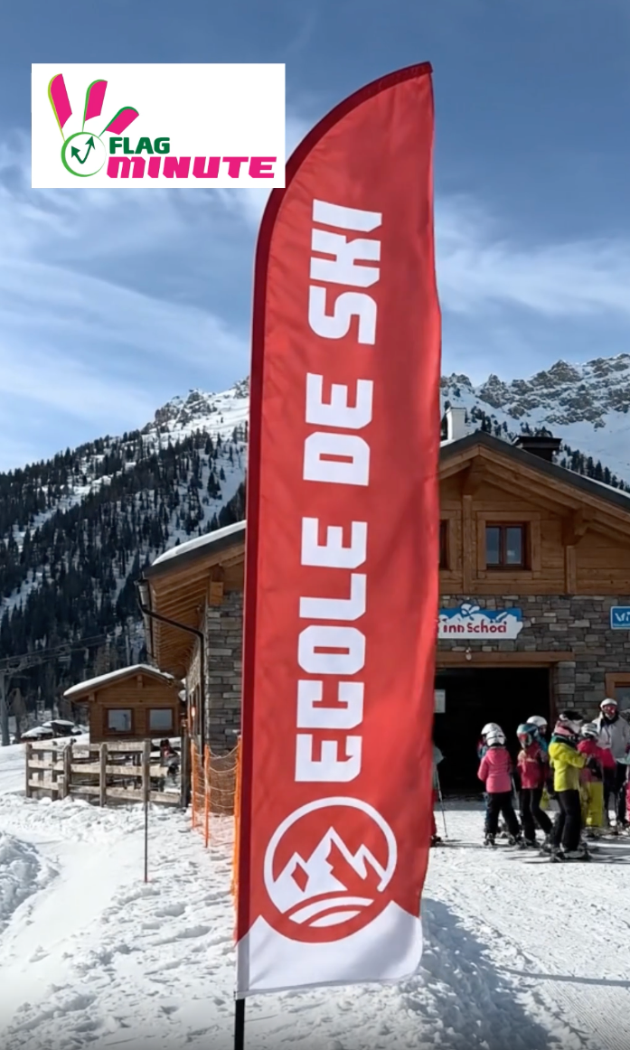 Vidéo du drapeau publicitaire 'École de Ski' rouge et blanc avec inscription en lettres blanches et logo de montagne, installé sur un pied lesté, idéal pour attirer les clients en station de ski.